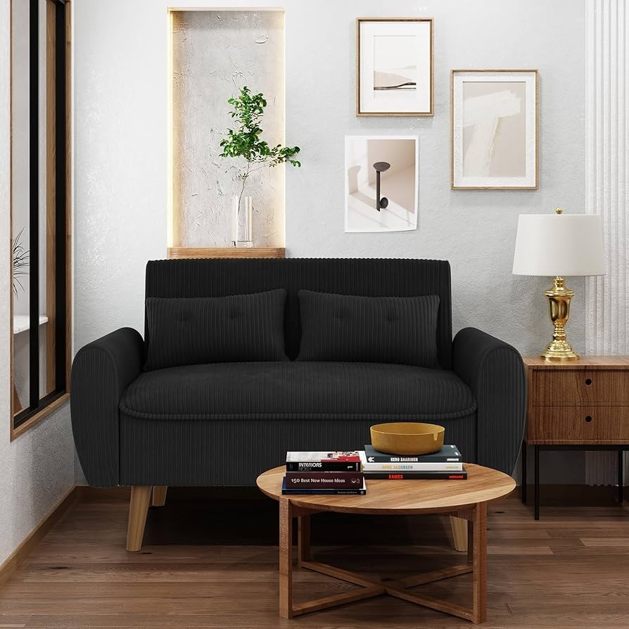 Modern black loveseat in a small living room with round coffee table and wall art.