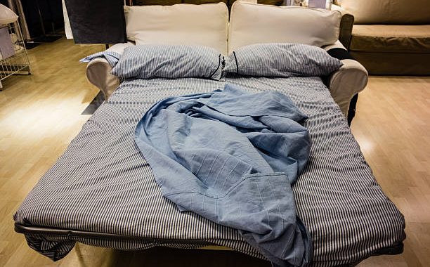an opened sofa bed with bed clothes and pillows