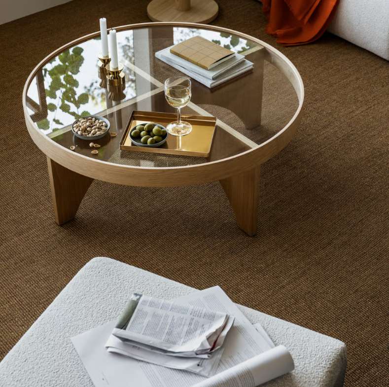 a round glass coffee table near a sofa, with candles, foods, a glass of drink and some books on it