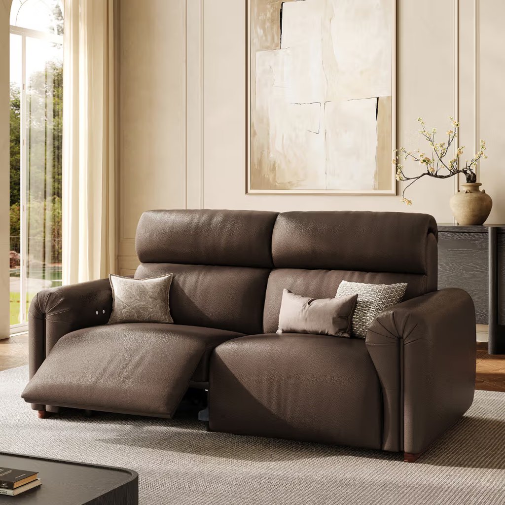 Brown leather reclining sofa with extended footrest in a modern living room with abstract wall art and natural light.