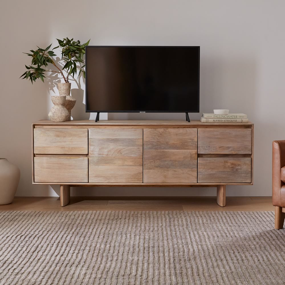 a brown wood media console with drawers for storage, a tv, some books and a plant on top near a sofa in a bright living room