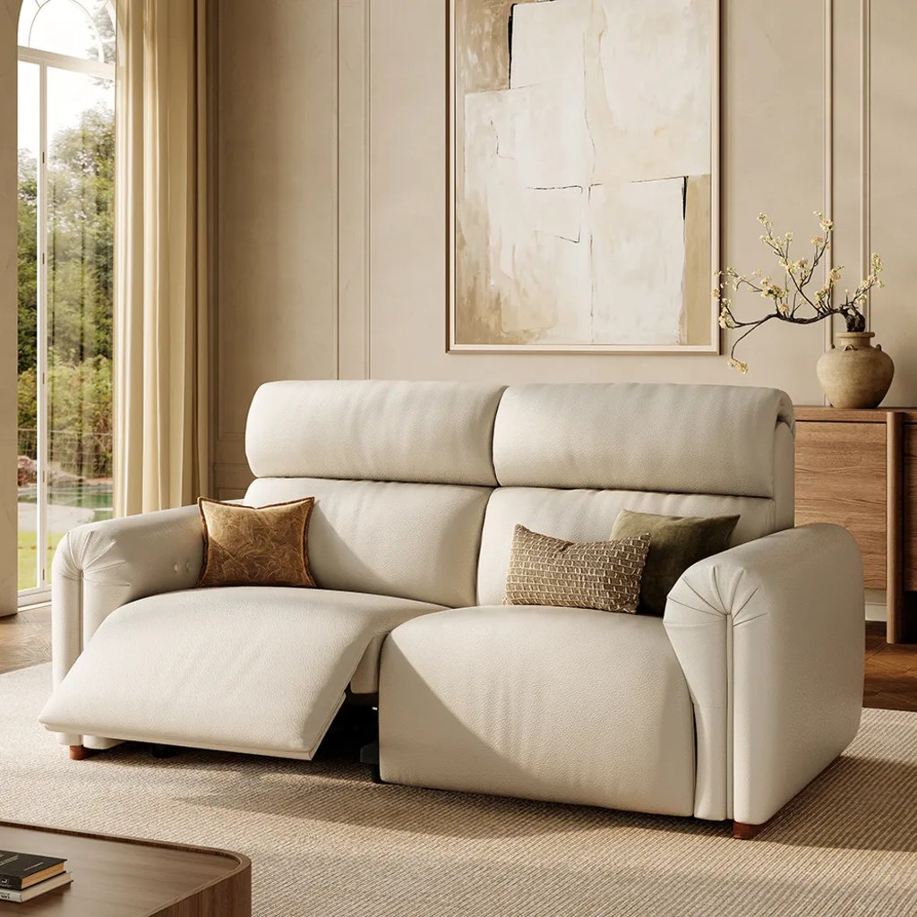 Cream leather power reclining loveseat with high back cushions and extended footrests in a bright living room.