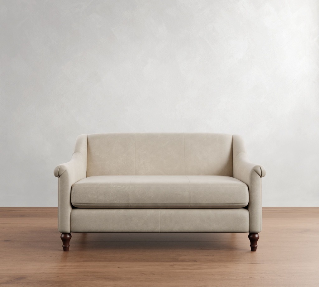 Compact cream leather loveseat with slim arms and dark wood legs against a plain wall.