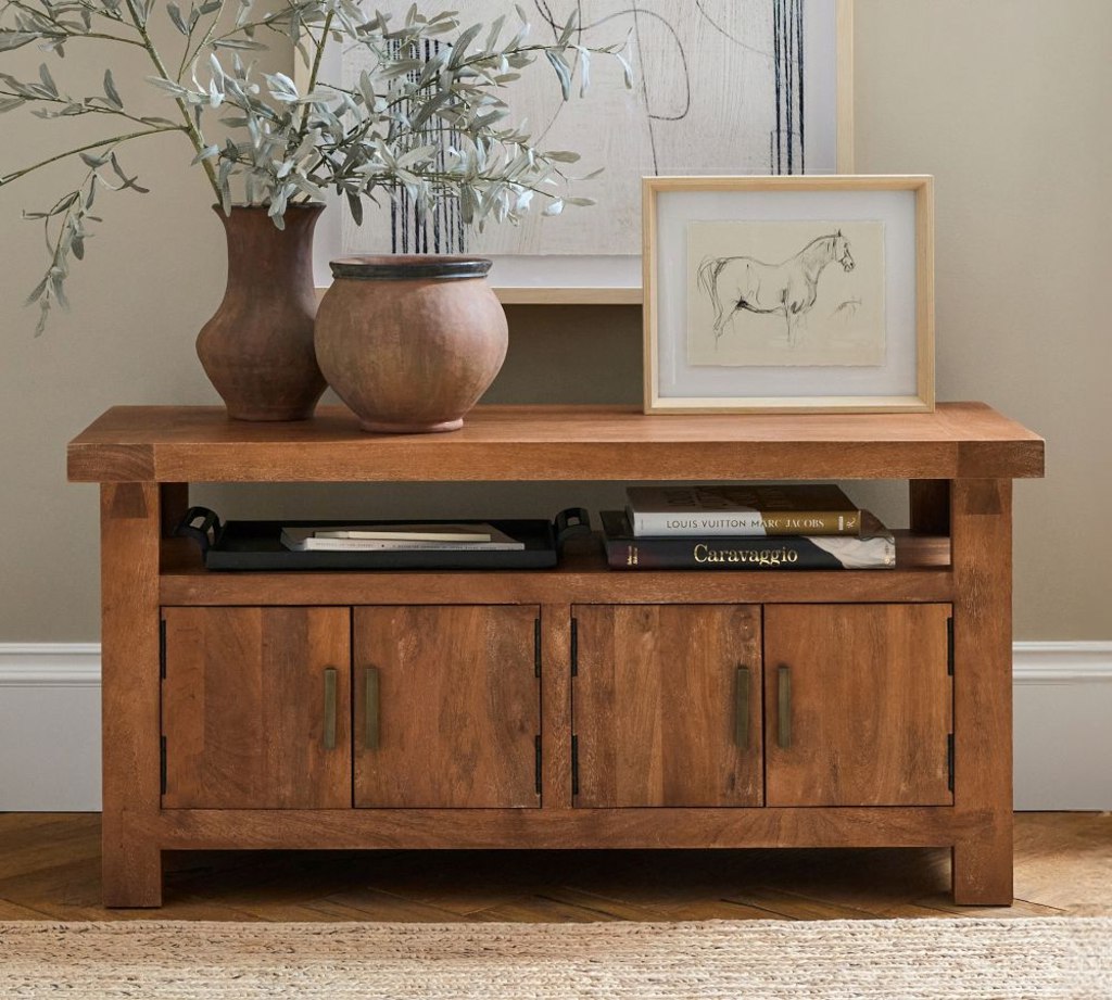 Wood media console with an open shelf and four cabinet doors, styled with vases, books, and framed art.