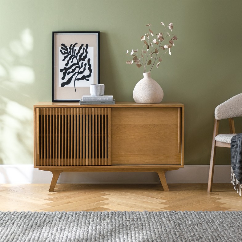 a wood tv stand with books and decorations on top near a chair in a modern and bright living room
