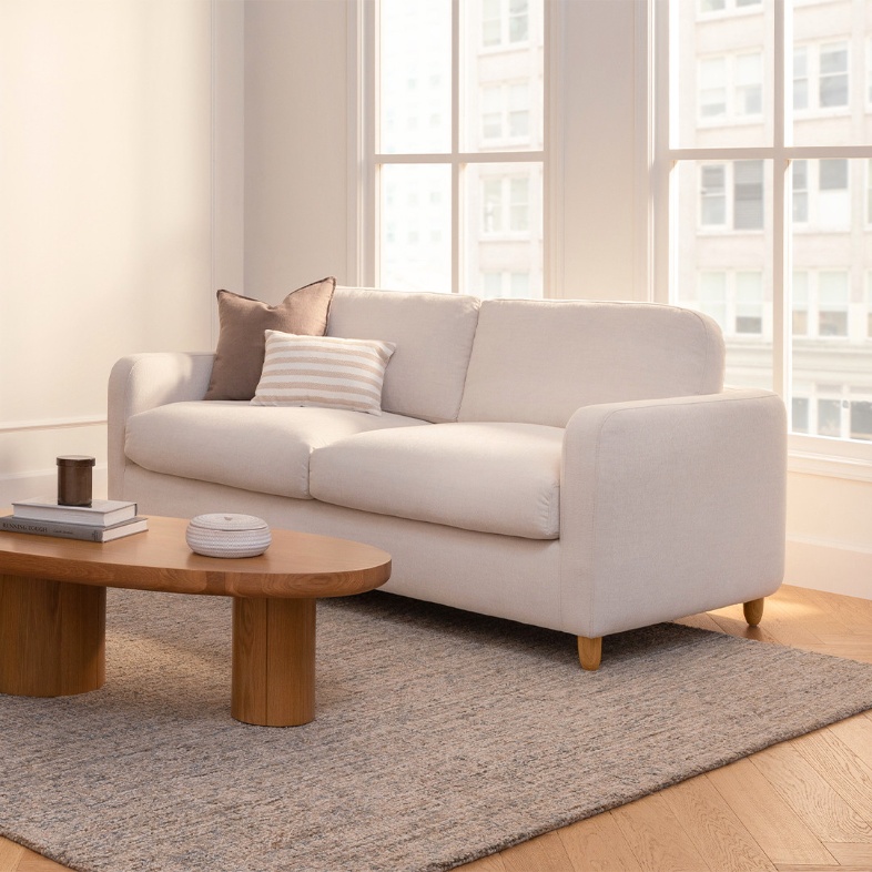 a white leather sofa bed near a wood coffee table in a bright and compact living room