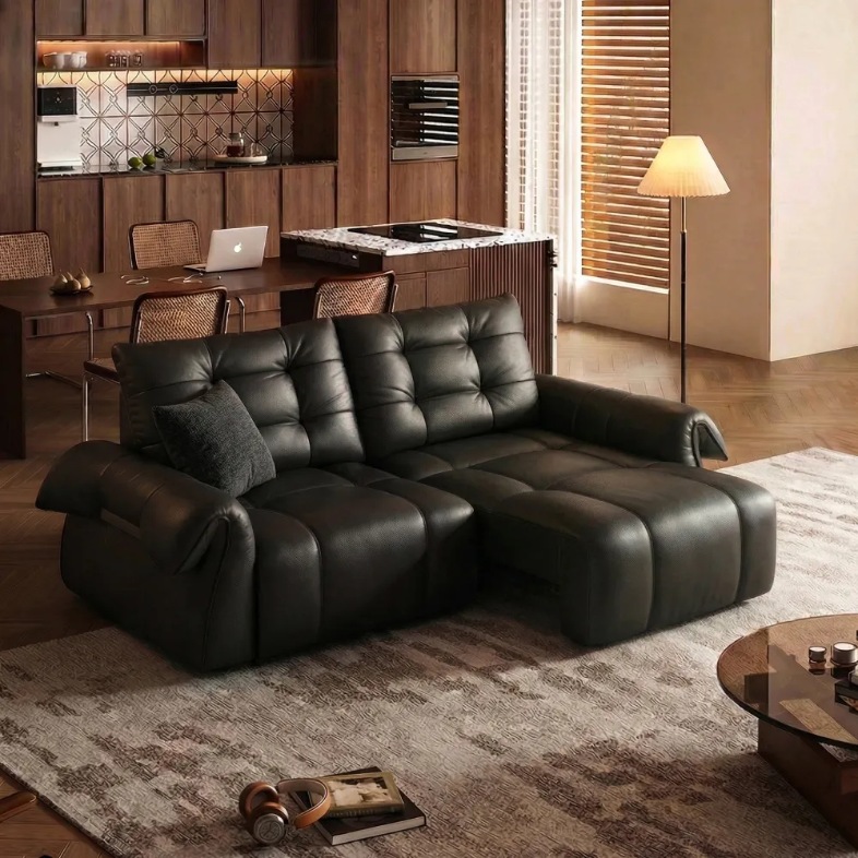 a black leather power sofa bed with a cushion near a coffee table and a dining table in a living room