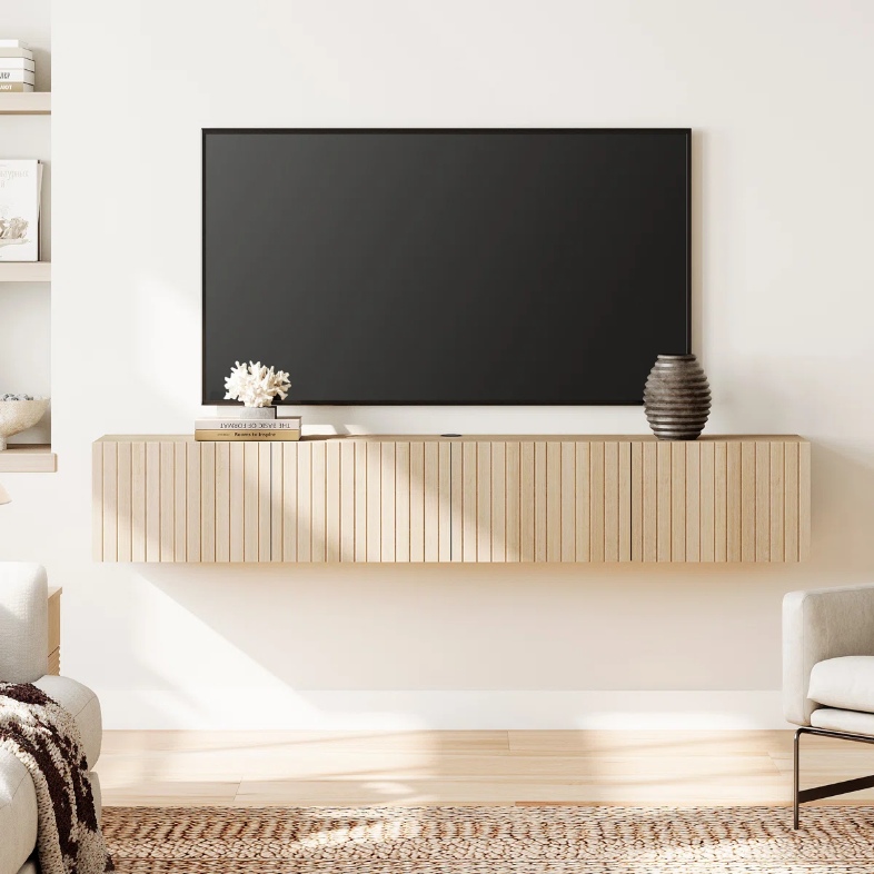 a light wood floating media console with books and decorations on top for tv stand near a sofa in a modern living room