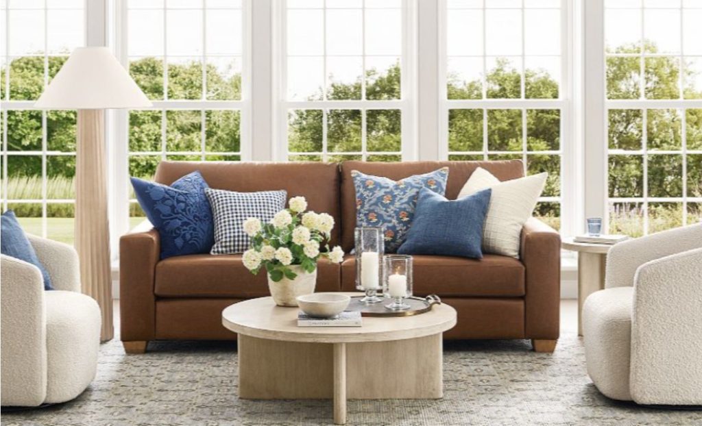 a tan colour-like leather sofa with cushions near a coffee table in a bright room