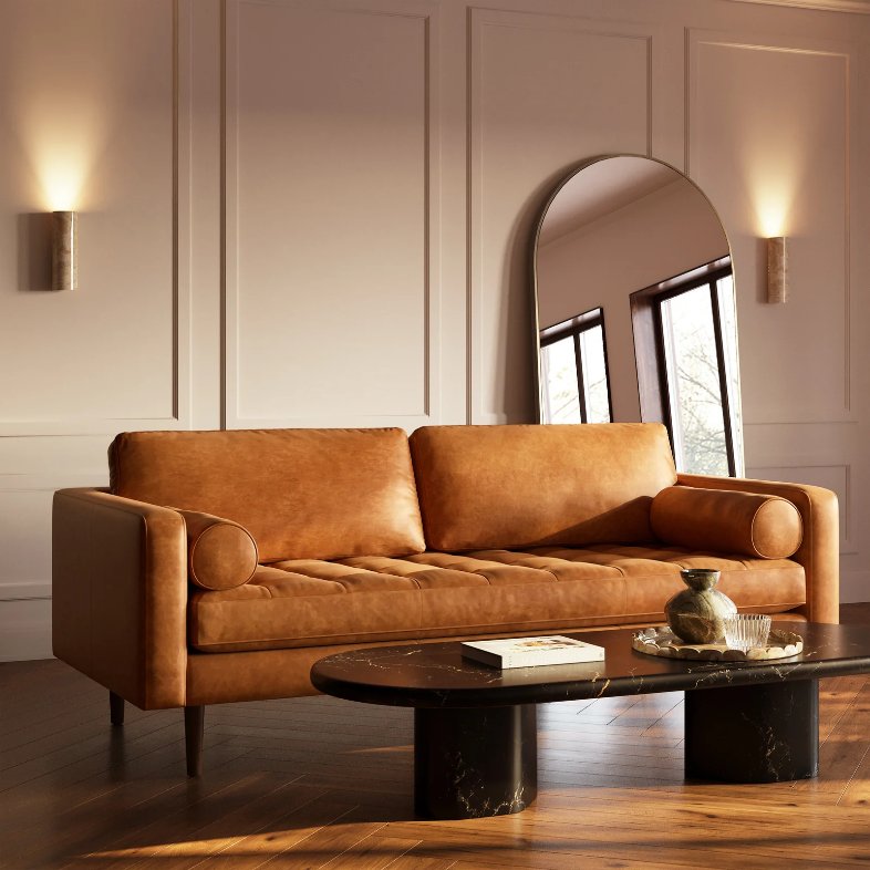 a Poly & Bark Napa Leather Sofa with square arms and roll cushions near an oval marble coffee table and a mirror in a bright and minimalist living room