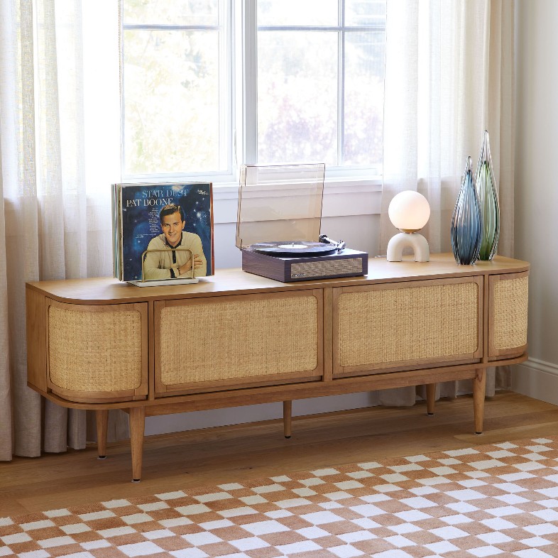 World Market Colby Rustic Sienna and Herringbone Rattan Media Stand with storage and disc, a disc player and decorations on top in a bright living room