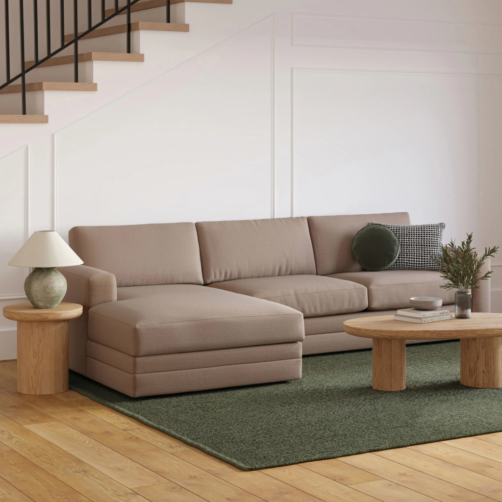 Beige chaise sectional sofa in a modern living room with a green area rug, wood coffee table, and staircase.