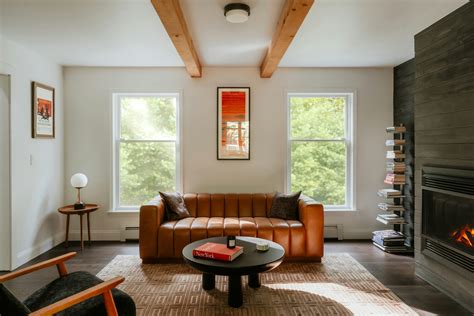 a luxurious leather sofa near a round black coffee table, a side table with a lamp, a bookshelf, a chair and a fireplace in a bright and minimalist living room