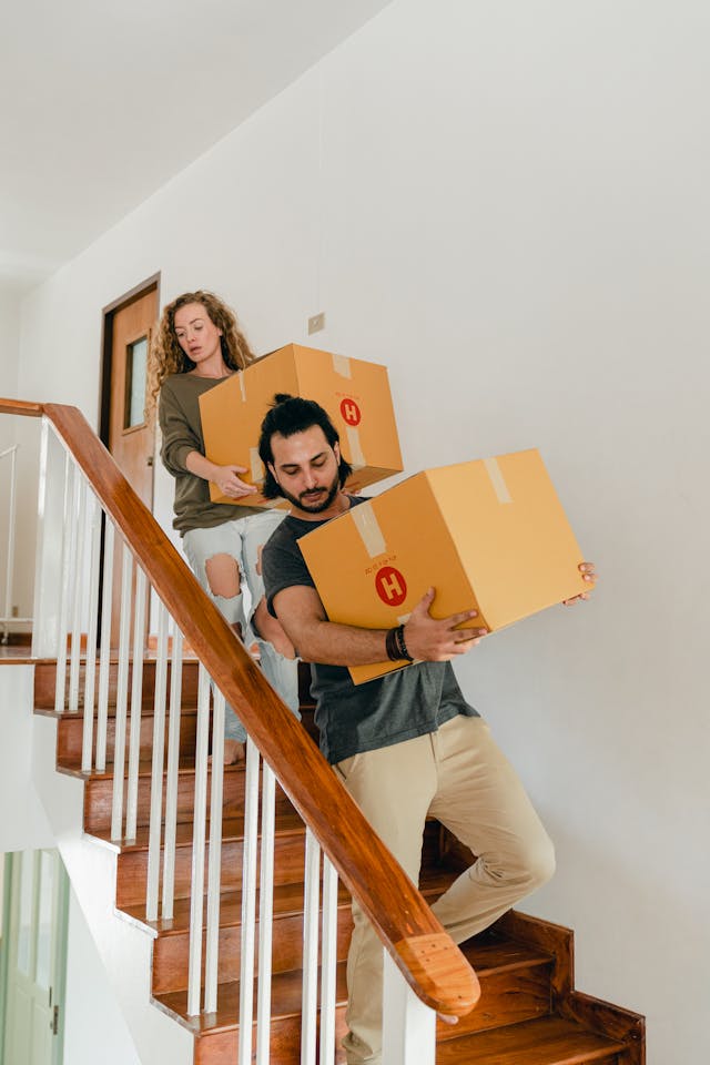 A young couple carrying boxes down stairs in a modern home