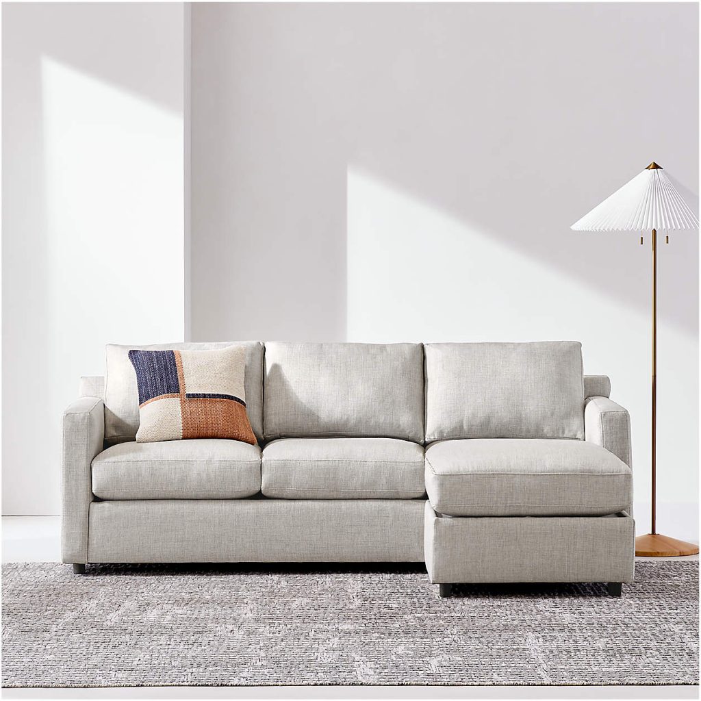 Crate & Barrel Barrett II Reversible Storage Chaise Lounge Queen Sleeper Sectional Sofa with chaise and cushion near a floor lamp in a bright living room