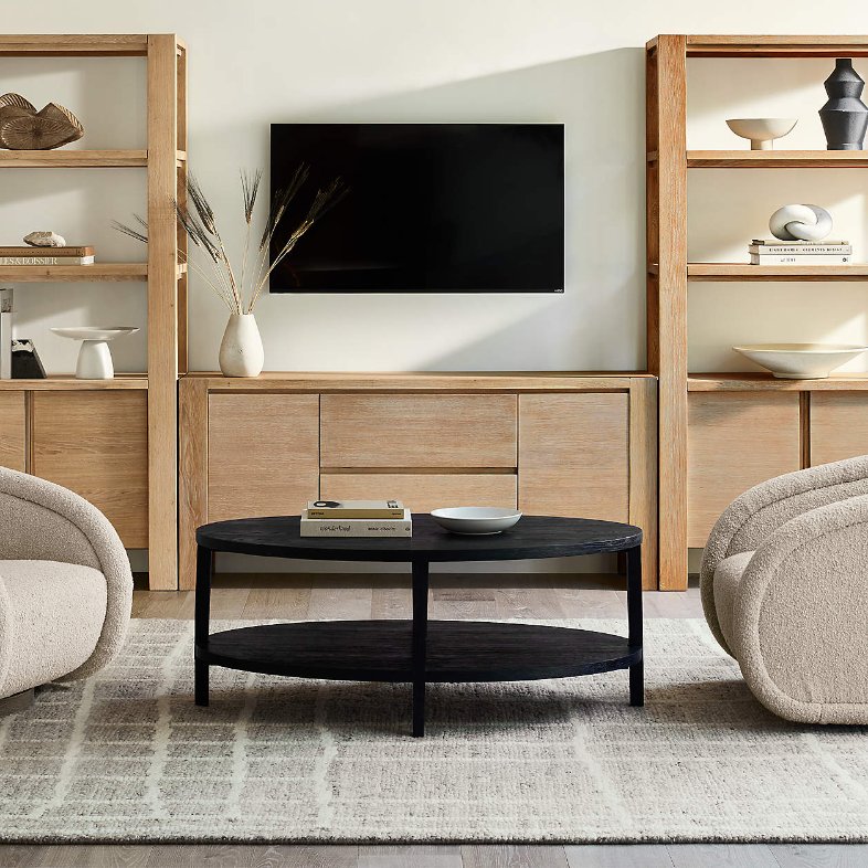 Crate & Barrel Terra 68" Natural Oak Wood Storage Media Console with drawers between two wood shelves near a round glass coffee table and sofas in a bright living room