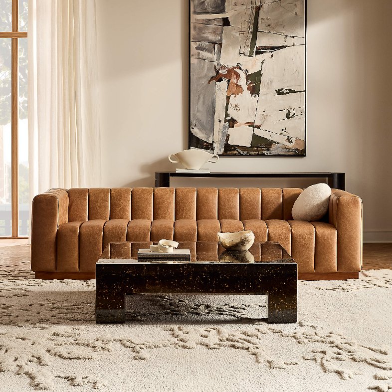 CB2 Forte 101" Extra-Large Channeled Saddle Leather Sofa near a rectangular marble coffee table and a black cabinet below a mounted painting in a bright and modern living room