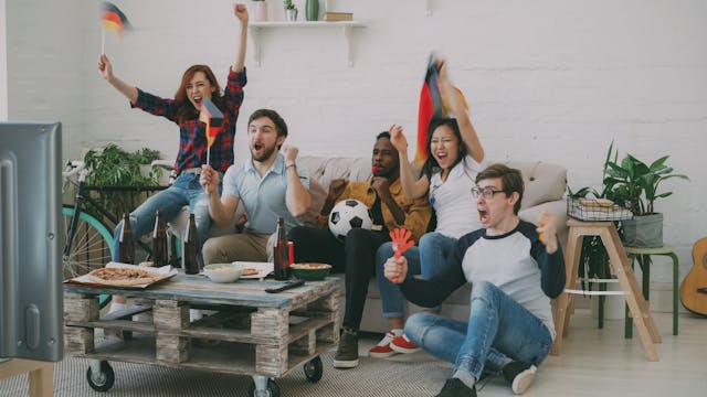 Group of friends celebrating while watching a live soccer match indoors