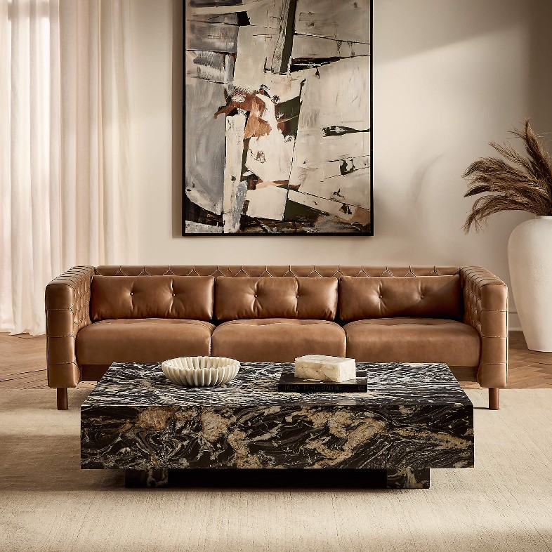 CB2 Marconi 81.5" Tufted Saddle Leather Sofa by Gianfranco Frattini near a rectangular marble coffee table and a plant in a  bright living room