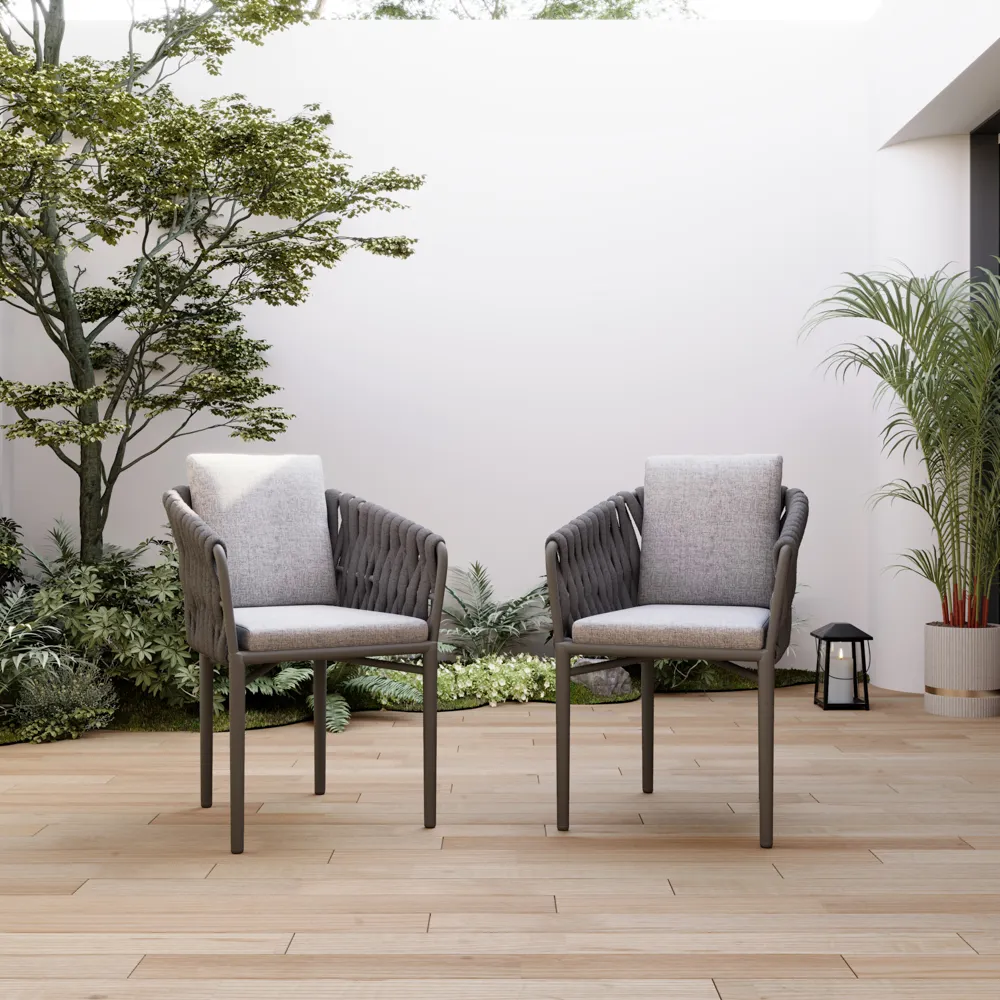 Two black wicker outdoor chairs around a small balcony table, with neutral cushions, a railing planter, and soft evening lighting.