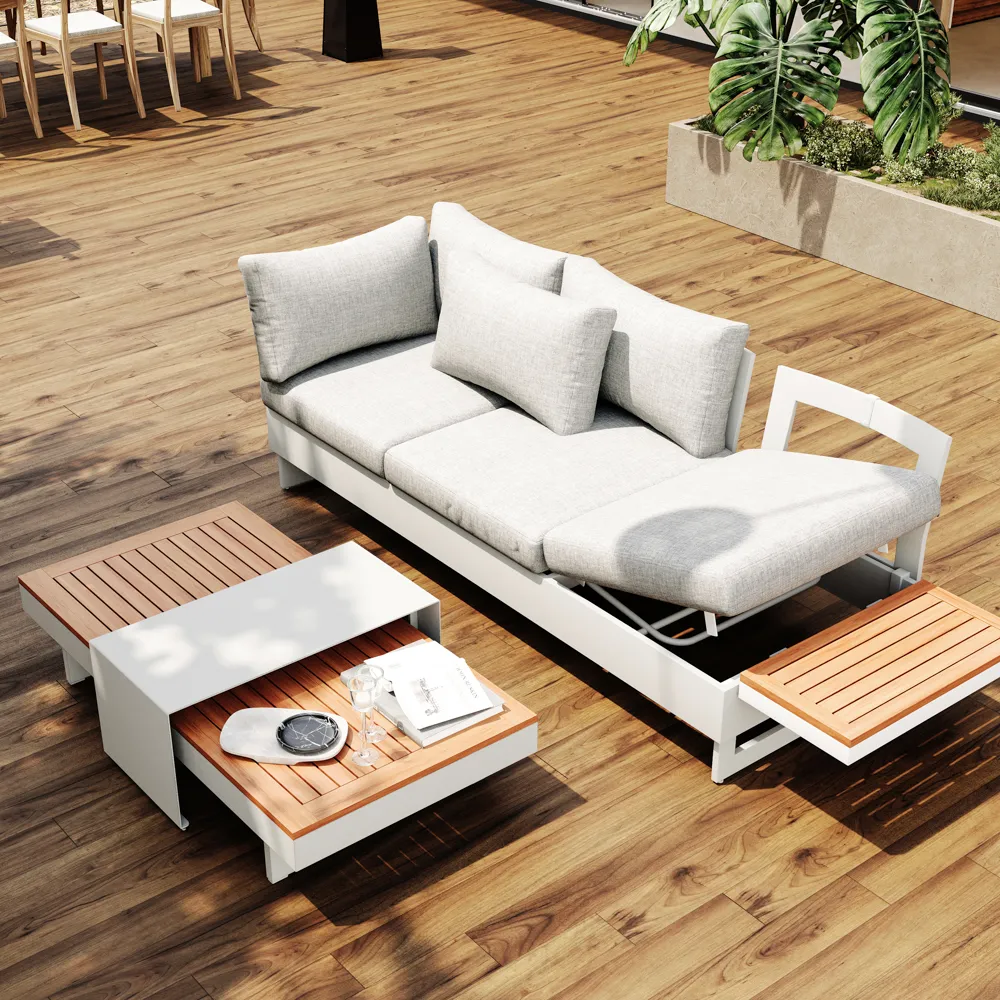 A gray outdoor sofa with a side table on a larger apartment balcony, styled with cushions, plants, and a tray for drinks.