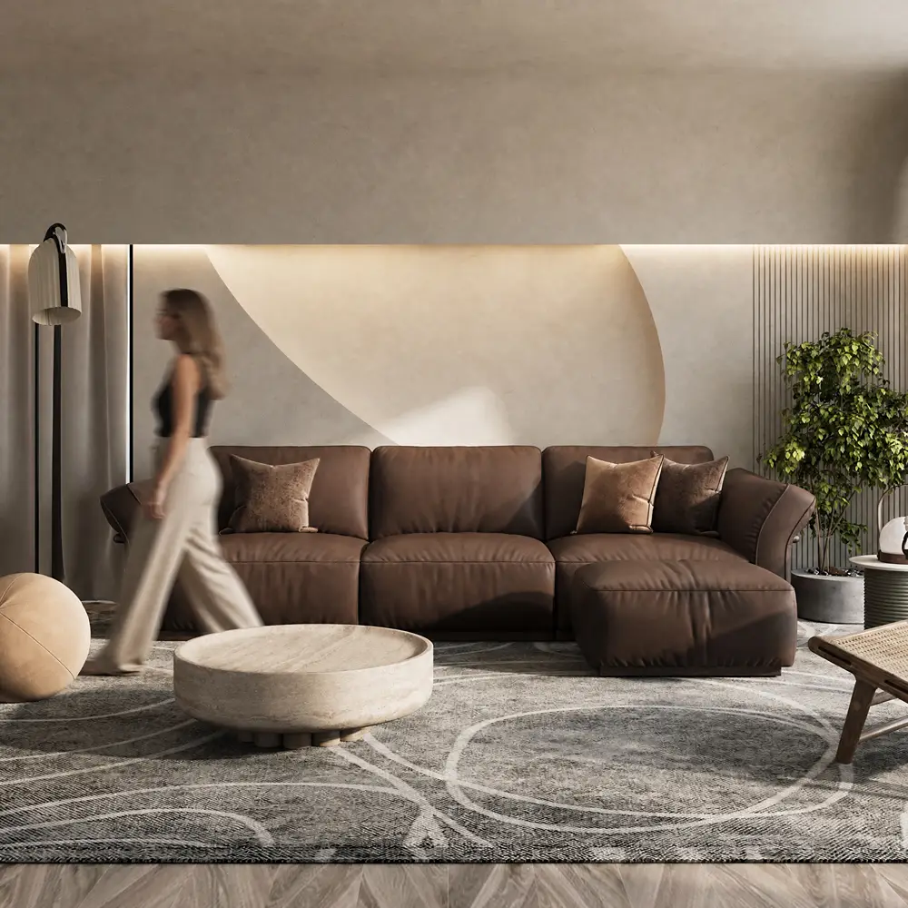 Dark brown leather sectional sofa with a right-facing chaise lounge and accent pillows in a modern living room with a round stone coffee table.