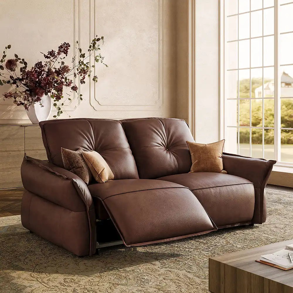 Dark brown leather power reclining loveseat with one extended footrest, tufted back cushions, and accent pillows in a sunlit living room.