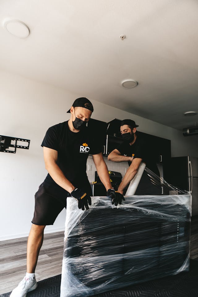 Two masked men moving a securely wrapped item in a modern room