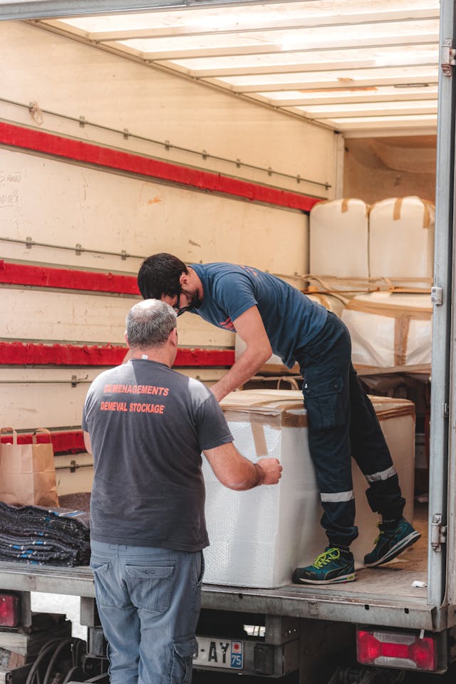 Two workers organizing furniture cargo inside a delivery truck