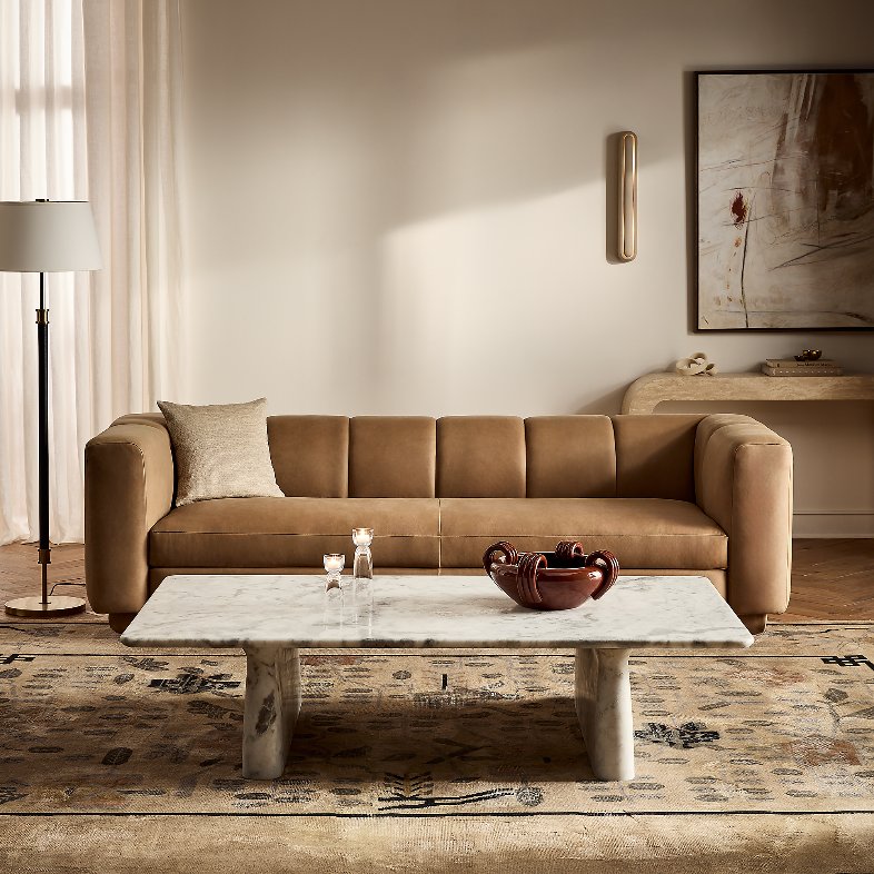 CB2 Yarrow 97" Brown Leather Sofa with a cushion near a rectangular marble coffee table and a floor lamp in a bright and modern living room