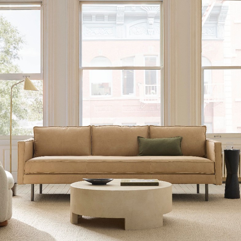 West Elm Axel Khaki Leather Sofa near a low round white coffee table, a black side table and a floor lamp in a bright and modern apartment