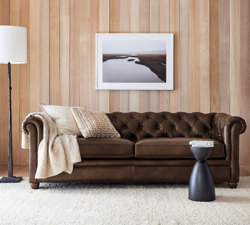 Pottery Barn Chesterfield Roll Arm Tufted Leather Sofa with cushions near a floor lamp in a bright and minimalist living room