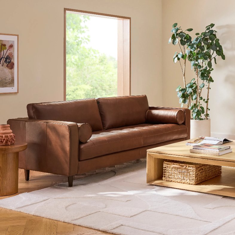 Article Sven 88" Tufted Leather Sofa near a rectangular wood coffee table, a round wood side table and a plant in a minimalist and bright living room