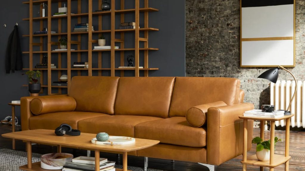 a Burrow Block Nomad Leather Sofa near a rectangular wood coffee table, a wood side table and a shelf in a  bright living room