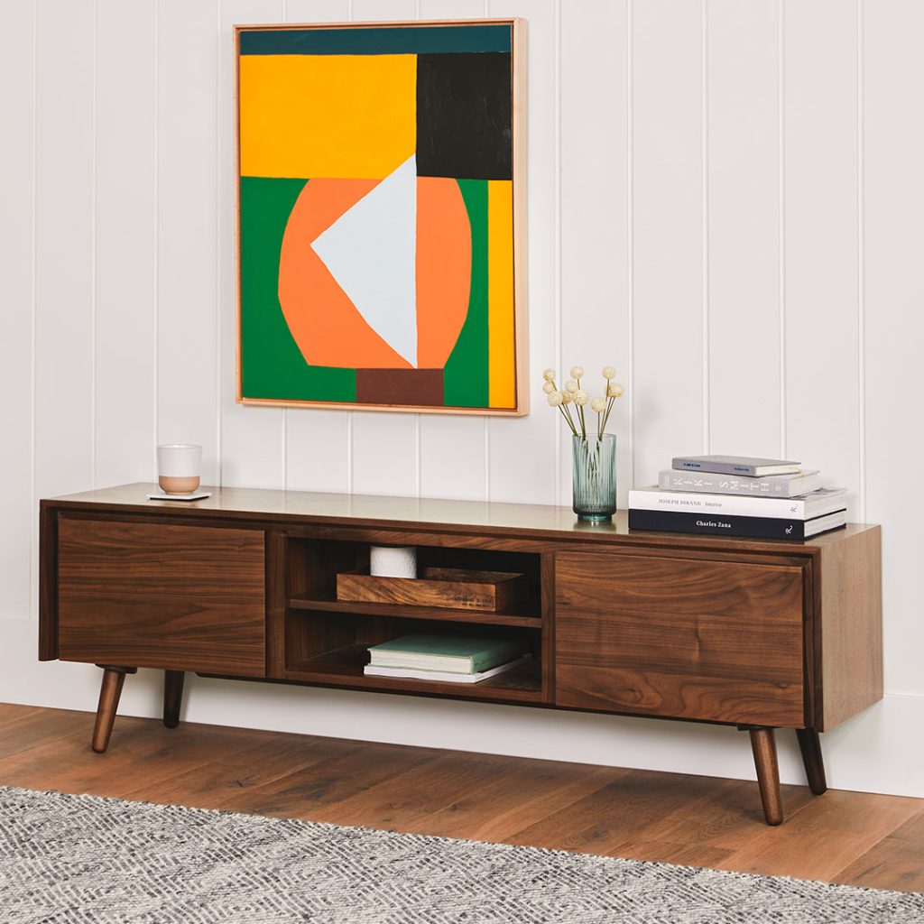 Article Seno 63" Low Media Unit with storage for books and decorations on top below a mounted painting in a modern mid-century living room