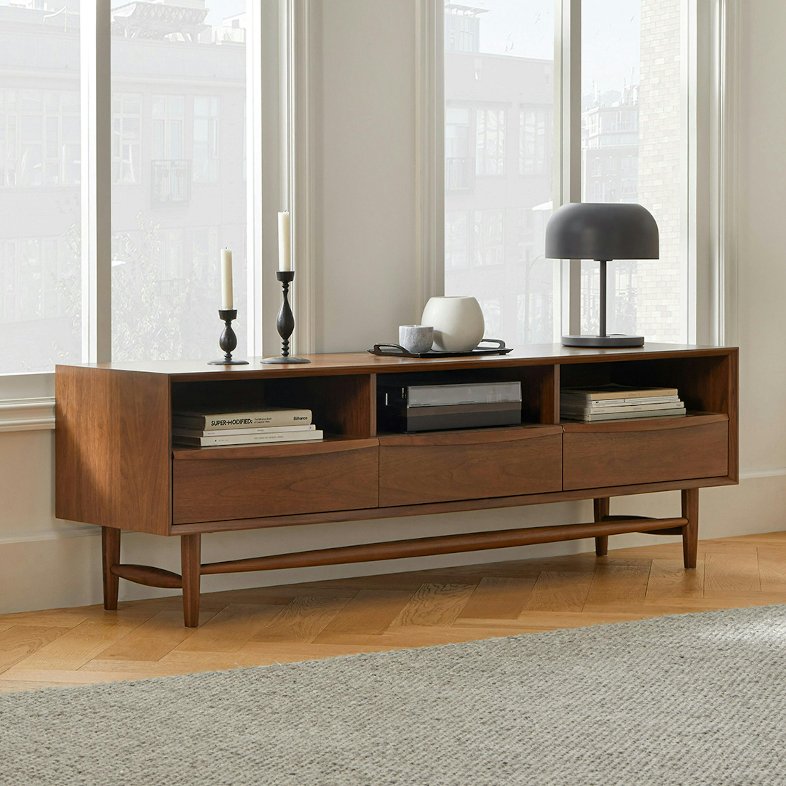 Article Lenia 63” low wood media console with storage for books, game play and media in a bright and modern living room with candles, a lamp and other decorations on top