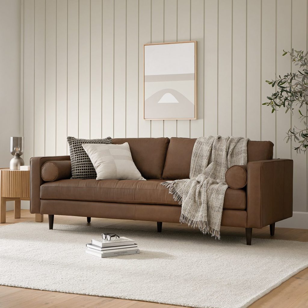Article Sven 88" Tufted Leather Sofa — Charme Chocolat with square arms and roll cushions near a plant and a round side table in a mid century modern living room