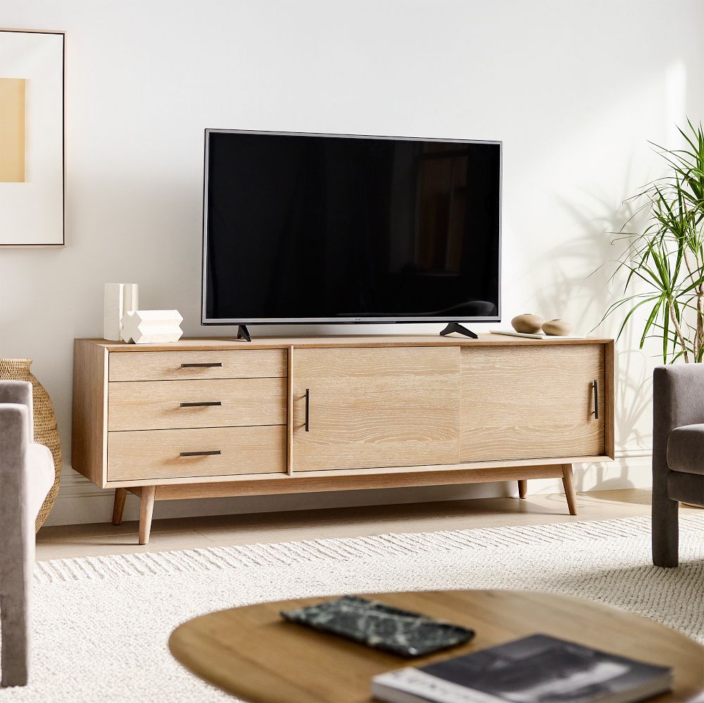 West Elm Mid-Century Media Console with drawers, slide doors storage for game play and media and a tv and decorations on top near a plant and two sofas in a bright sitting room