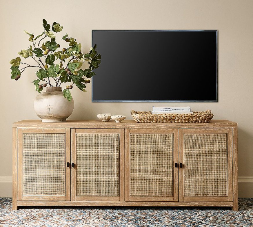 Pottery Barn Modern Farmhouse Cane Media Console with storage and decorations on top below a black mounted tv in a bright room