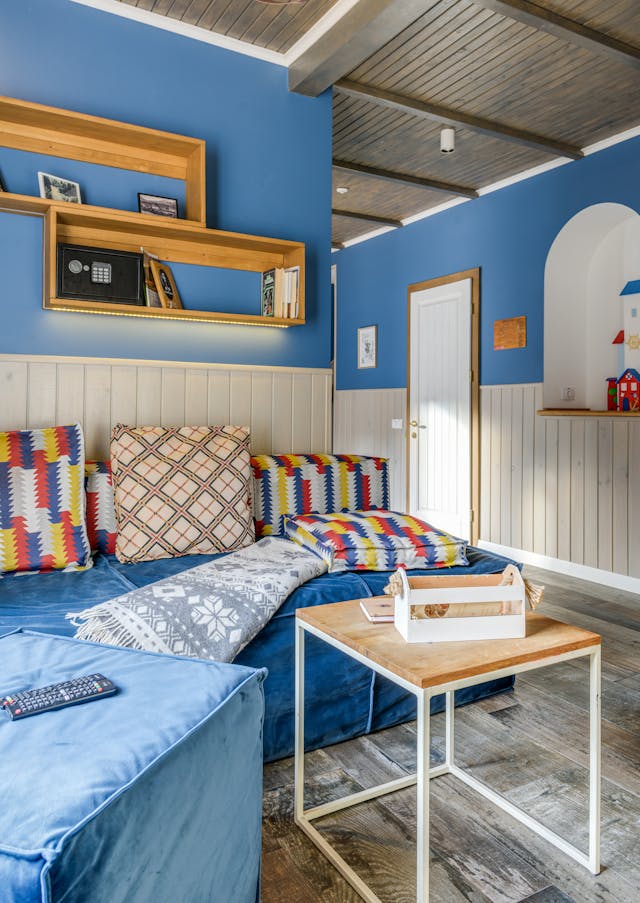 Stylish living room interior featuring a blue sofa, patterned cushions, and contemporary shelves.