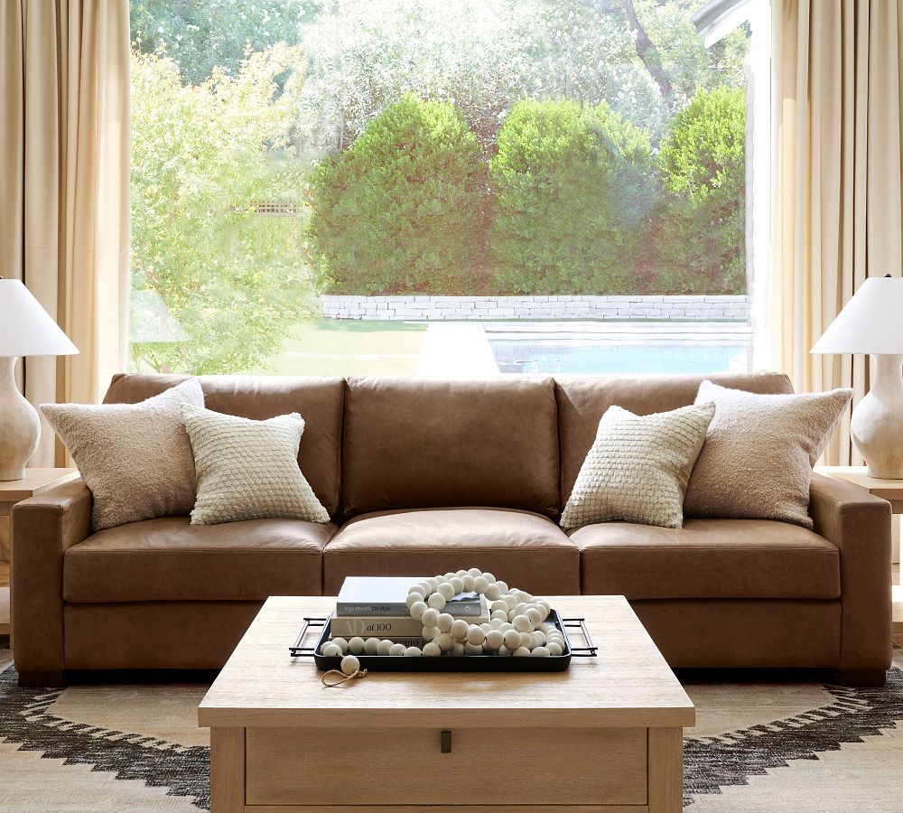 Pottery Barn Turner Square Arm Leather Sofa with square arms and cushions near a rectangular wood coffee table, two side tables  with lamps in a bright and modern living room