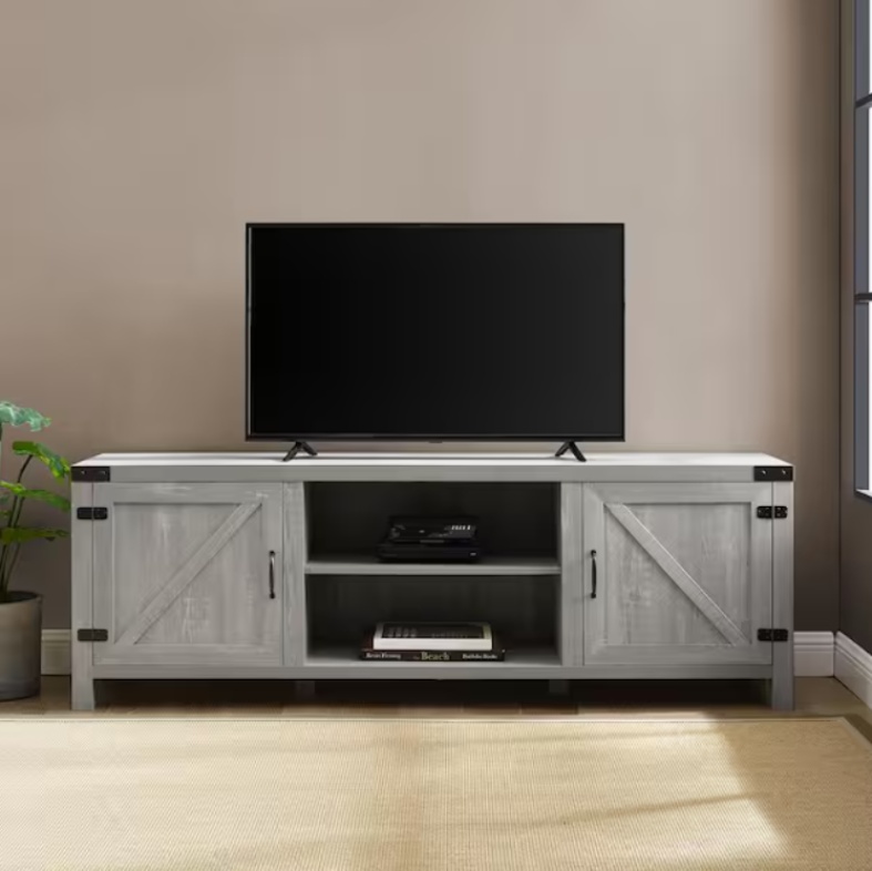 Walker Edison 70" Modern Farmhouse Barn Door TV Stand with slide doors and storage for books and a video projector near a plant and a tv in a bright and cozy living room