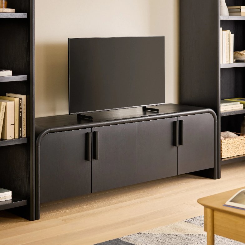 Article Faydra 70” Media Unit - Black with storage and a tv on top between black shelves with books in a modern and minimalist living room