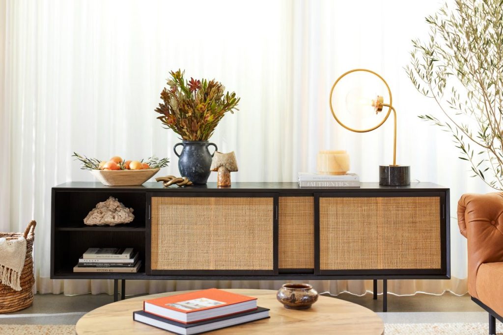 Joybird Oslo Media Console with slide door storage for books and decorations and a lamp and plants on top near a leather sofa, a round wood coffee table and a plant in a bright living room
