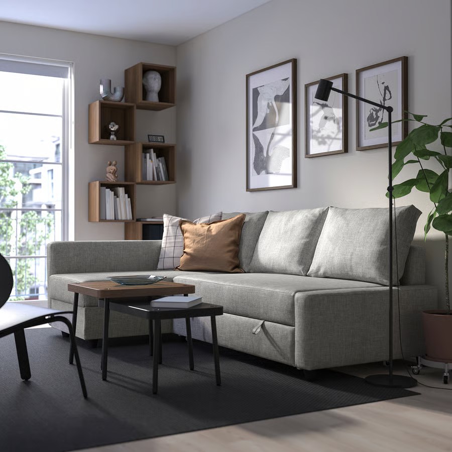 IKEA FRIHETEN Sleeper Sectional with Storage and chaise near a coffee table, an accent chair, a plant, a floor lamp and a bookshelf in a bright and modern living room