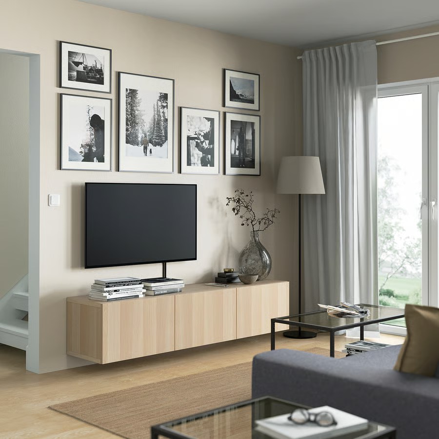 IKEA BESTÅ TV Unit with Doors for storage and some books and decorations on top below a wall-mounted tv in a bright and modern mid-century living room