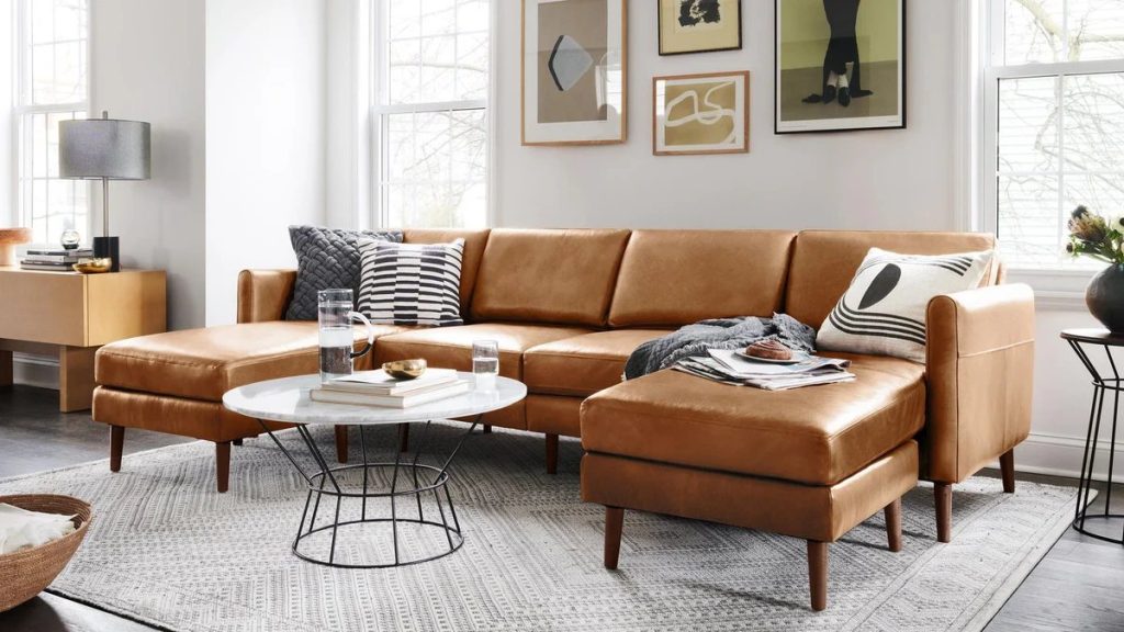 Burrow Nomad brown Leather Sofa with modular chaise and cushions near a round marble coffee table, a side table and a console table in a bright and minimalist living room