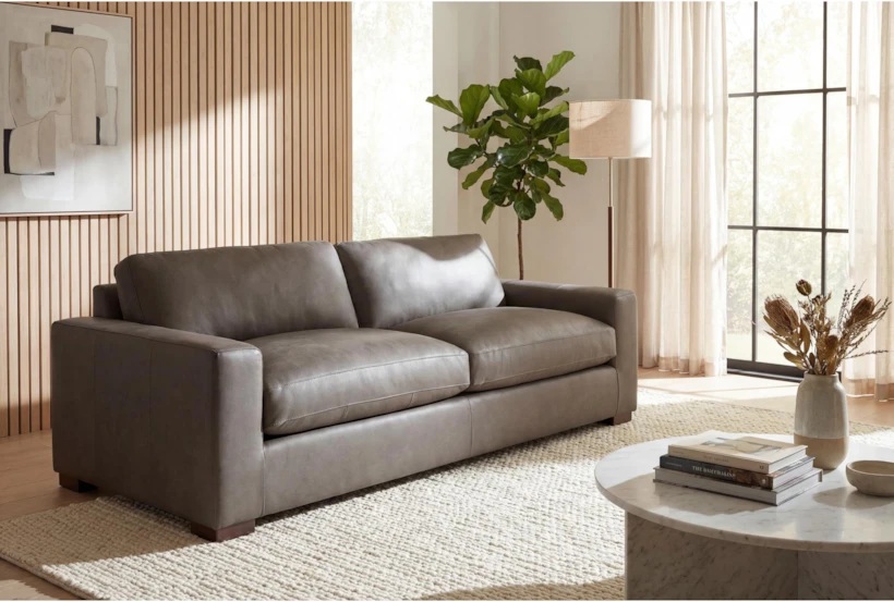 Living Spaces Mason II Chocolate Leather Sofa with square arms and cushions near an oval marble coffee table, a floor lamp and a plant in a bright and minimalist living room