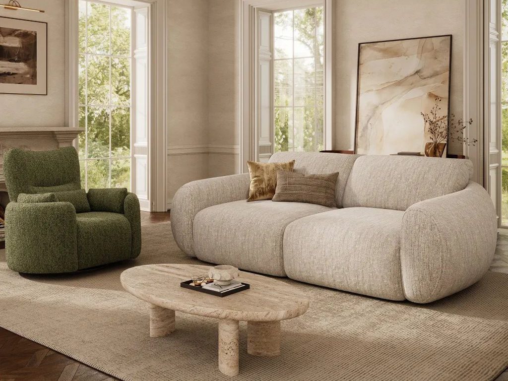 a beige sofa bed and a green accent chair near an oval marble coffee table and a wood console table with a painting on top in a luxurious and bright living room