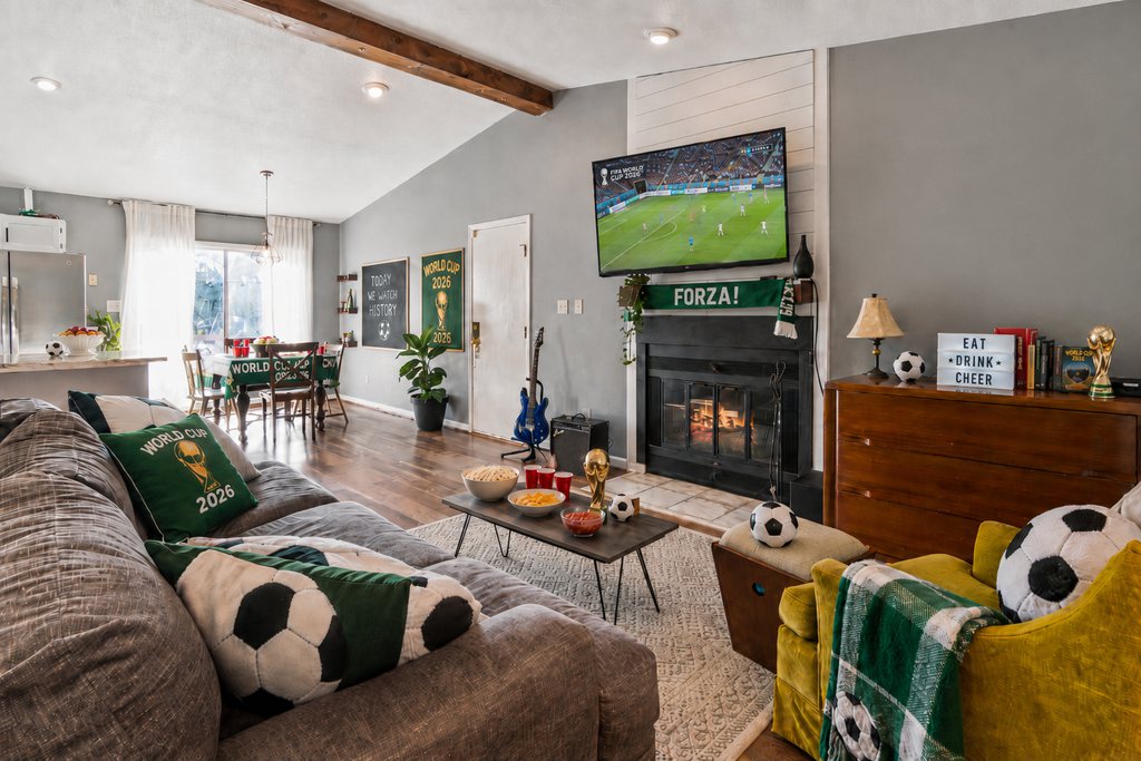 World Cup watch party setup in an open concept living room with a sectional sofa, coffee table snacks, TV stand, dining area, and soccer-themed decor.
